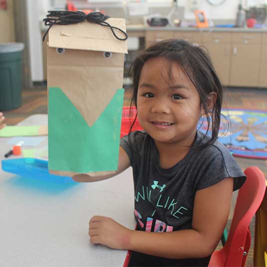 Camper holding puppet made from brown paper bag with green construction paper